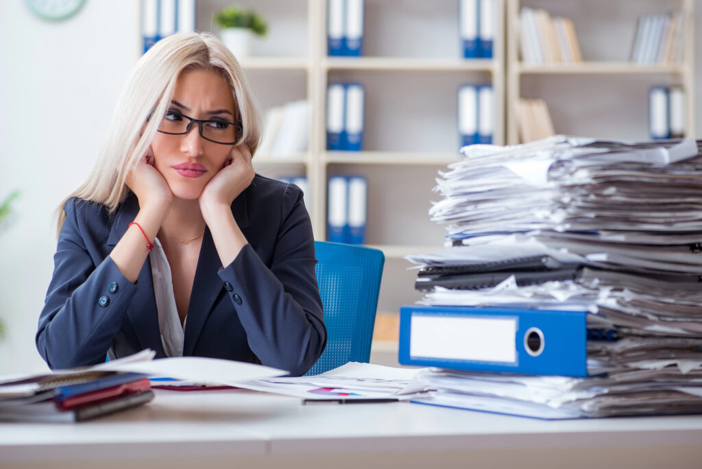 Stressed female accountant sitting at a desk stacked with paperwork